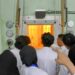Ruang dengan kaca tebal dan lampu oranye kemungkinan adalah ruang hot cell atau reaktor mini, tempat reaksi nuklir atau penanganan material radioaktif berlangsung secara aman. Dinding dan panel besi tebal merupakan pelindung radiasi.