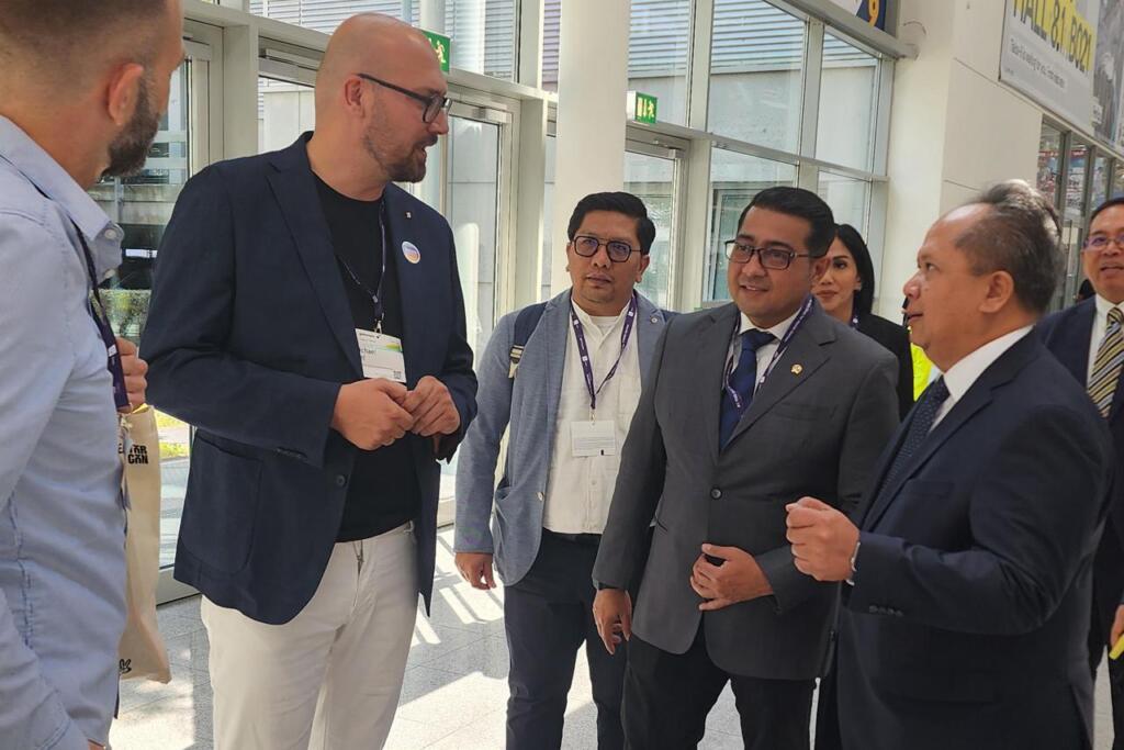 Menteri Ekraf Bawa Semangat Perkuat Ekosistem Game Nasional di Jerman 3 A group of professionals engaged in conversation indoors, with a bright, modern setting and large windows in the background.