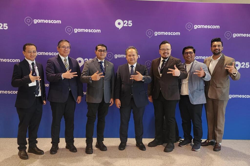 Menteri Ekraf Bawa Semangat Perkuat Ekosistem Game Nasional di Jerman 4 A group of seven men in suits poses together in front of a purple Gamescom backdrop, making hand gestures.