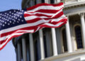 The flag of the united states of america flying in front of the capitol building blurred in the background. United states federal congress on Capitol hill in Washington D.C. Democracy and freedom.
