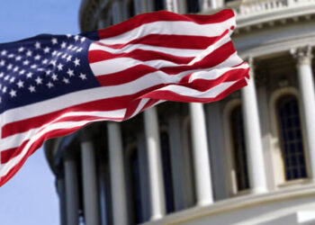 The flag of the united states of america flying in front of the capitol building blurred in the background. United states federal congress on Capitol hill in Washington D.C. Democracy and freedom.