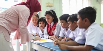 A female Malay teacher and her students participating in a group discussion inside a classroom.