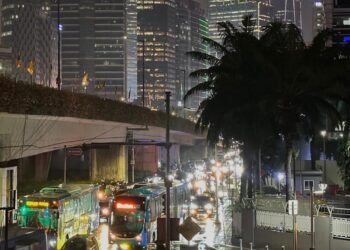 Hujan Deras Sore Hari Sempat Timbulkan Kemacetan di Jl. Sisingamangaraja, Kini Lalu Lintas Kembali Normal 48 Pemandangan jalanan kota Jakarta di malam hari yang basah karena hujan, dengan gedung pencakar langit, bus, dan lampu kendaraan yang memantul di aspal.