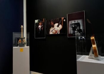 Jakarta, 20 November 2025 — Indonesia Music Summit 2025 yang berlangsung pada 19–20 November di Taman Ismail Marzuki (TIM), Jakarta, menghadirkan sejumlah agenda, salah satunya pameran musik yang dipusatkan di Galeri Emiria Soenassa. Pameran ini menampilkan arsip musik, karya visual, hingga koleksi yang menggambarkan dinamika industri musik Indonesia dari masa ke masa. Sejak pagi, aliran pengunjung tampak stabil memasuki ruang galeri. Di bagian awal pameran, pengunjung disambut oleh deretan foto musisi legendaris Indonesia dari Rhoma Irama hingga Nike Ardilla yang dipajang disana. Sorotan lampu galeri membuat setiap detail mulai dari foto lawas sampai ekspresi panggung terlihat jelas dan hidup. Di sisi lain ruang pameran, meja panjang menampilkan buku-buku bertema musik yang sedang banyak dibicarakan publik maupun pelaku industri. Beberapa judul yang dipamerkan antara lain buku mengenai hak cipta musik, laporan tentang kondisi pekerja ragam gender di ekosistem seni dan kreatif, serta panduan mengenai festival musik ramah lingkungan. Beberapa siswa tampak membaca ringkasan konten buku atau mendiskusikannya dengan rekan mereka. Di sudut lain, area pameran gitar hasil lomba menghias dan melukis menjadi titik paling mencuri perhatian. Deretan gitar yang diberi motif batik, lukisan abstrak, hingga desain modern berwarna cerah membuat banyak laki-laki yang berpenampilan seperti seniman berhenti untuk mengamati detail visual dan mengambil foto. Tak kalah menarik adalah etalase kaca berisi koleksi kaset jadul dari dekade 70-an hingga 90-an. Sampul kaset yang mulai memudar namun masih ikonik menarik minat banyak pengunjung. Sebuah pemutar kaset tua yang mengalunkan cuplikan lagu-lagu klasik Indonesia menambah suasana autentik tanpa berlebihan. “Melalui arsip visual, koleksi fisik, dan literatur musik, kami ingin menghadirkan ruang belajar sekaligus ruang apresiasi. Musik berkembang bukan hanya dari panggung, tetapi juga dari kerja keras para pekerja seni di belakangnya,” ujar Rani, salah satu panitia acara. Selama dua hari penyelenggaraan, pameran di Galeri Emiria Soenassa menjadi salah satu acara yang paling ramai dikunjungi dalam Indonesia Music Summit 2025. Banyak pengunjung terlihat menikmati pameran sambil berdiskusi, menunjukkan antusiasme terhadap literasi dan sejarah musik tanah air.