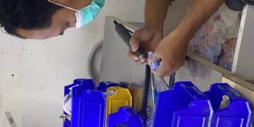 Teknisi gigi sedang merapikan gigi tiruan menggunakan alat laboratorium.