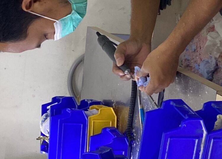 Teknisi gigi sedang merapikan gigi tiruan menggunakan alat laboratorium.