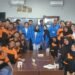 Sebuah foto grup di dalam ruang kelas. Di bagian tengah, delapan mahasiswa PkM UBSI mengenakan jaket almamater biru berbaris dan duduk. Mereka dikelilingi oleh lebih dari dua puluh siswa SMKT Kapin yang mengenakan seragam polo oranye-hitam. Semuanya berpose dan tersenyum ke arah kamera.