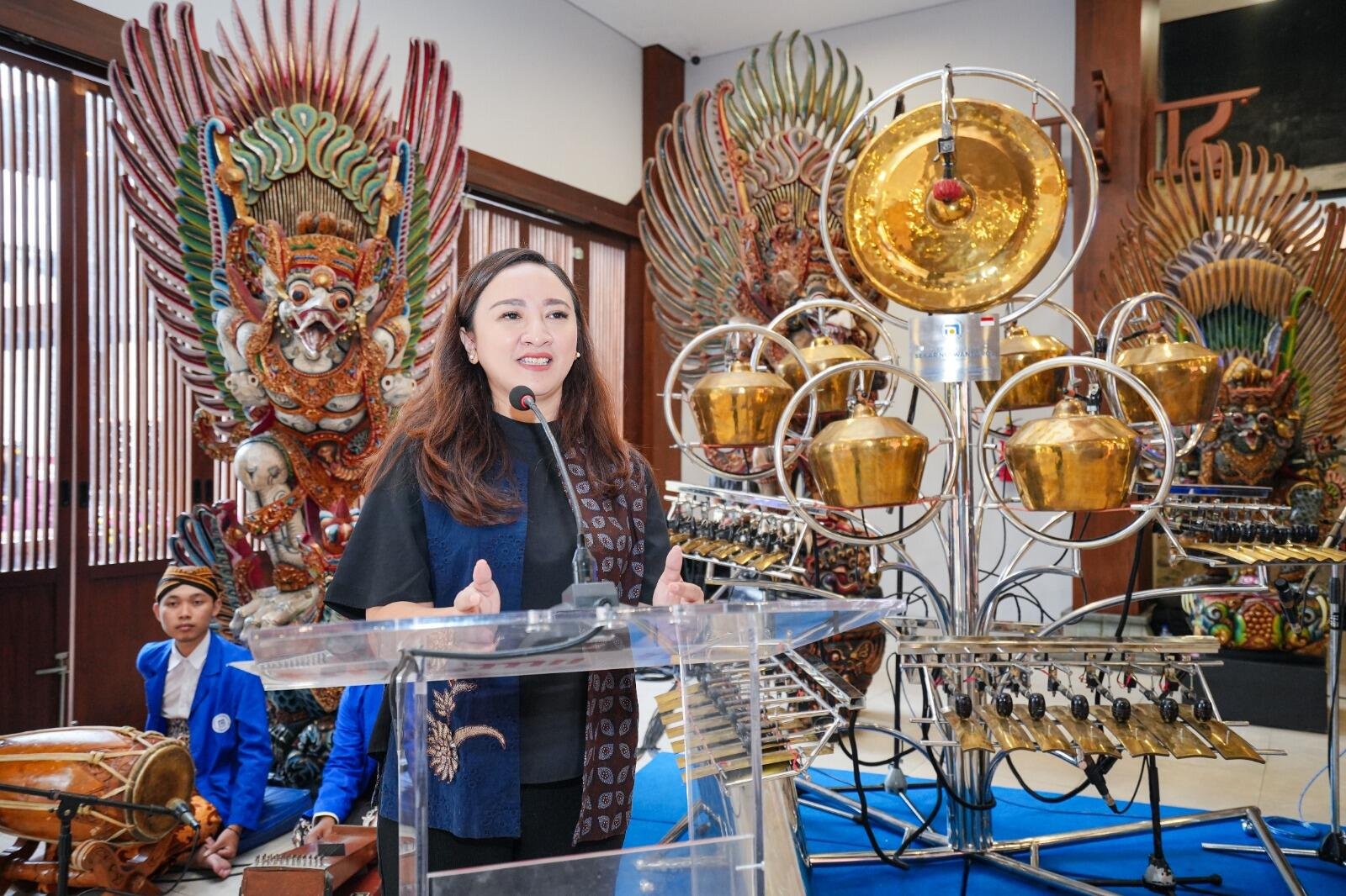 Kementerian Ekraf Luncurkan Robot Gamelan di TMII, Apresiasi Teknologi dan Tradisi 48 A woman speaks at a podium, with traditional musical instruments and ornate decorations in the background.