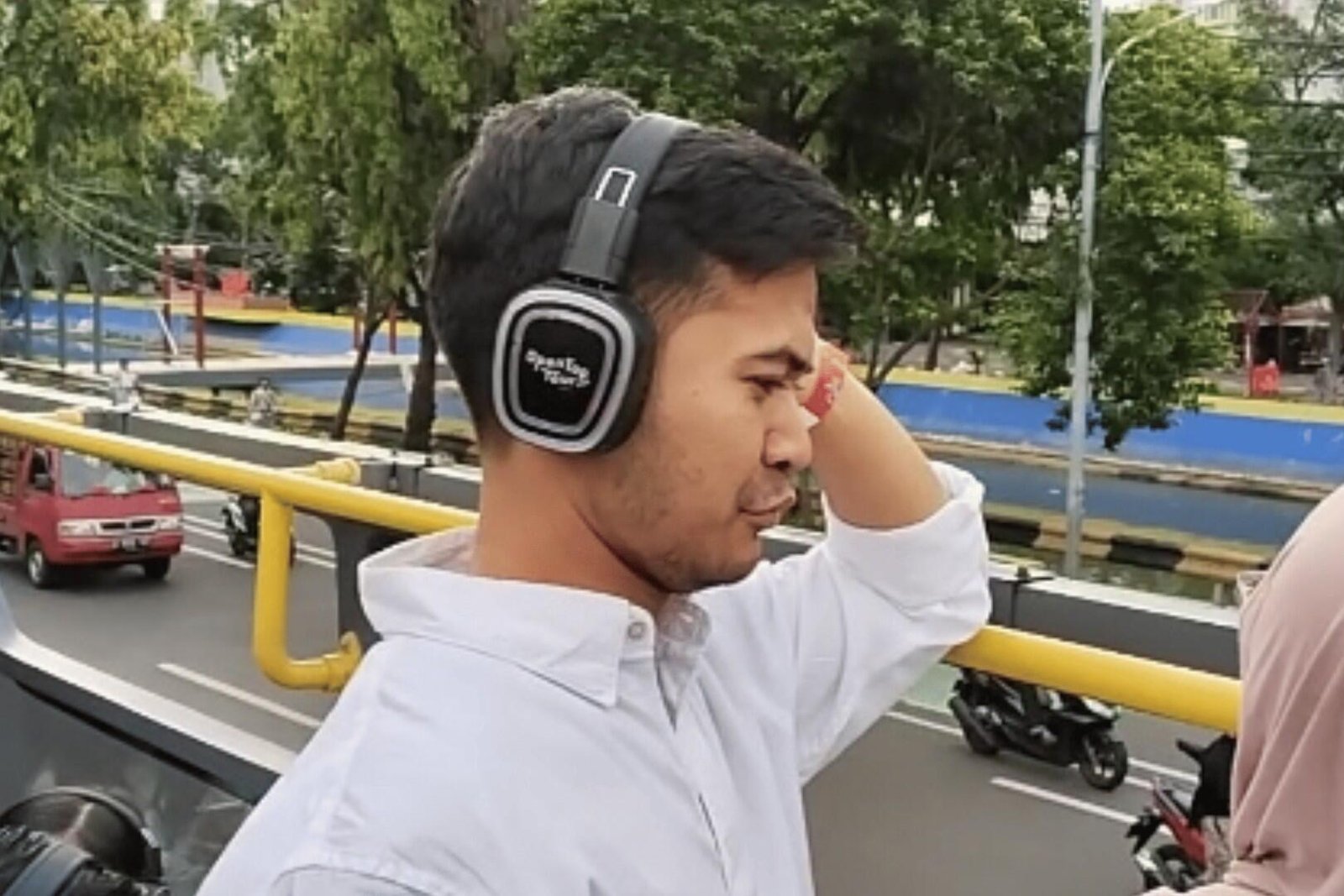 Penumpang pria sedang menggunakan silent headphones di atas dek bus atap terbuka Jakarta Heritage.