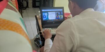 Mahasiswa UBSI Aulia Iskandar Lubis sedang melakukan serah terima website SDI AM FATWA secara daring melalui laptop yang menampilkan video conference dengan kepala sekolah.