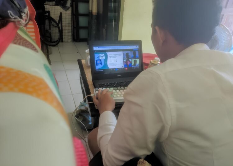 Mahasiswa UBSI Aulia Iskandar Lubis sedang melakukan serah terima website SDI AM FATWA secara daring melalui laptop yang menampilkan video conference dengan kepala sekolah.