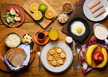 High angle view of abundant breakfast made at home in Sunday  a special day . In the image are healthy food ingredients as milk,apple-fruit egg,jam,cashew,granola,banana fruit,orange juice,orange fruit,cheese,butter,over rustic pine wood table in the kitchen.Image made in studio using a 24 megapixels full frame sensor camera.