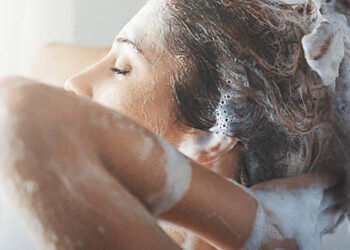 Perempuan sedang mencuci rambut dengan sampo, memijat kulit kepala dengan busa tebal, mencerminkan cara keramas yang benar untuk rambut sehat.