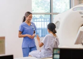 Keterangan foto: Ilustrasi radiografer perempuan yang bekerja menggunakan peralatan radiologi dengan menerapkan prosedur keselamatan radiasi untuk melindungi diri dari paparan radiasi saat bertugas. {Sumber: iStock).