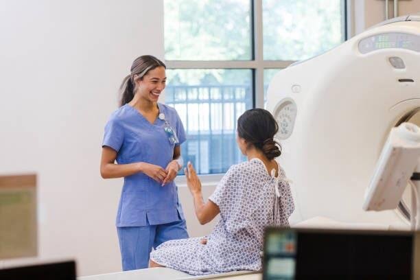 Keterangan foto: Ilustrasi radiografer perempuan yang bekerja menggunakan peralatan radiologi dengan menerapkan prosedur keselamatan radiasi untuk melindungi diri dari paparan radiasi saat bertugas. {Sumber: iStock).